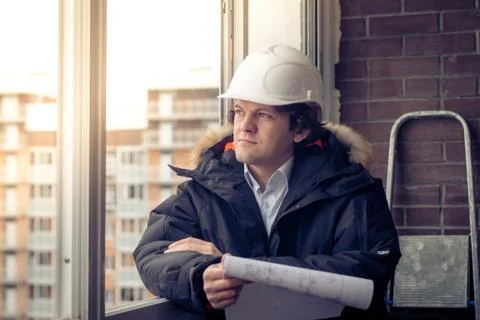 Pensive young man builder in hard hat standng and thinking. Soft focus, toned. Stock Photos