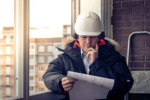 Pensive young man builder in hard hat standng and thinking. Soft focus, toned. Stock Photos
