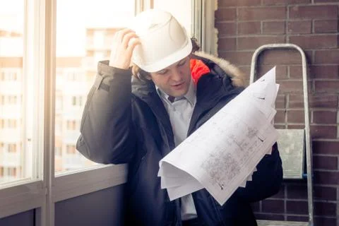 Pensive young man builder in hard hat standng and thinking. Soft focus, toned. Stock Photos