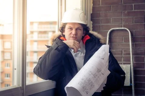 Pensive young man builder in hard hat standng and thinking. Soft focus, toned. Stock Photos