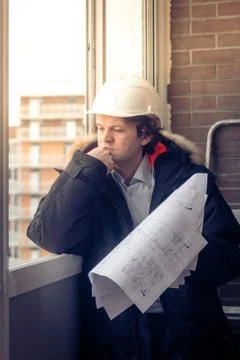 Pensive young man builder in hard hat standng and thinking. Soft focus, toned. Stock Photos