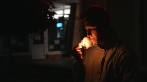 Pensive young man lights a cigarette with matches in the darkness on the street Видео 108123699