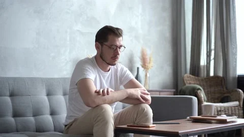 Pensive Young man Sitting on Sofa and Thinking at Home. Video stock 137955199