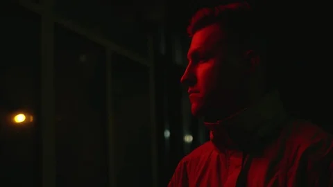 Pensive young man standing on the dark street at night and looking on the red Video stock 108123724