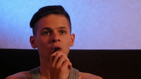 Pensive young man vaping on the sofa in the room 库存影片 106370334