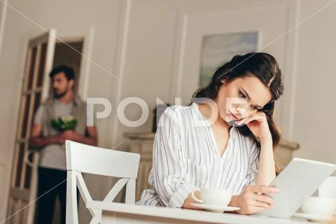 Pensive young woman sitting at table and using digital tablet at home Stock Photos