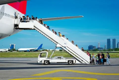 People are boarding from apron, by the stairs. Background city view. Stock Photos