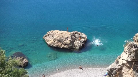 People are jumping from a large rock into the clear turquoise water of the Sea. Stock Footage 200918465