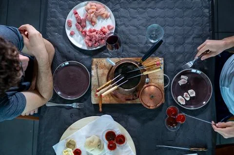 People are sitting at a table sharing a fondue bourguignonne meal, cooking .. Stock Photos