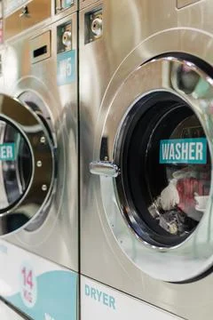 People are using washers and dryers at a laundromat. The machines are lined u Stock Photos