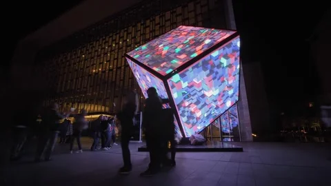 People are walking around the immersive LED cube installation art at night Stock Footage 339774367