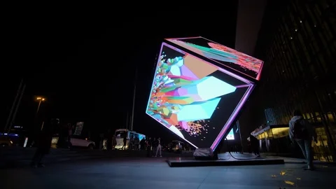 People are walking around the immersive LED cube installation art at night Stock Footage 339775896