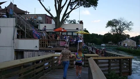 People are walking down a river lake bridge near the restaurant Stock Footage 78066441