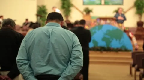 People bow their heads to pray while man speaking from church pulpit Stock Footage