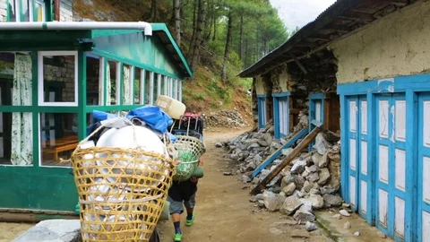People carrying items in big baskets through a narrow street between two houses Stock Footage 77445560