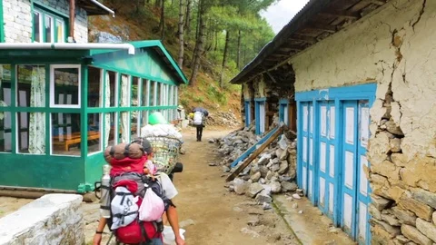 People carrying rucksacks and baskets walking through narrow path between houses Stock Footage 77445577