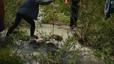 People cross muddy creek using sticks for support Stockbeeldmateriaal 333101693