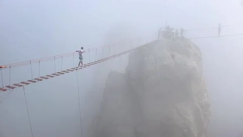 People crossing between rocks on a stretched wooden bridge in the fog Stock Footage 162726305