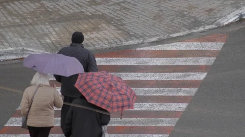 People crossing a pedestrian path with an umbrella on a rainy day Видео 106123729