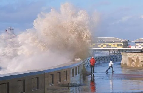People dodging  storm waves breaking over the sea wall at Blackpool Lancashir Stock Photos