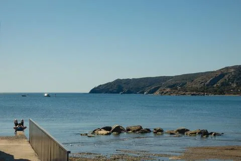 People enjoy their time by the water near rocks. Fotos Stock