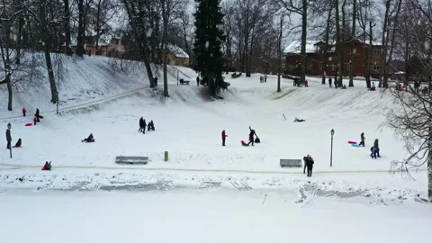 People enjoying sledding and playing in a snowy park during a winter snowfall Stock Footage 346594943