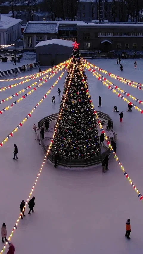People enjoying winter ice skating around a large decorated christmas tree with Vídeos de archivo 344848406