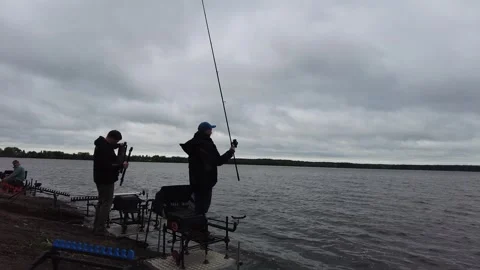 People fish by the lake on a cloudy day near the shore with fishing rods and cha Stock Footage 338332193