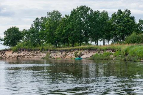 People float down a calm river in Europe in inflatable rubber boats. Stock Photos