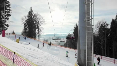 People go down the ski slope under the elevator in front of the mountains. Stock Footage 219003884
