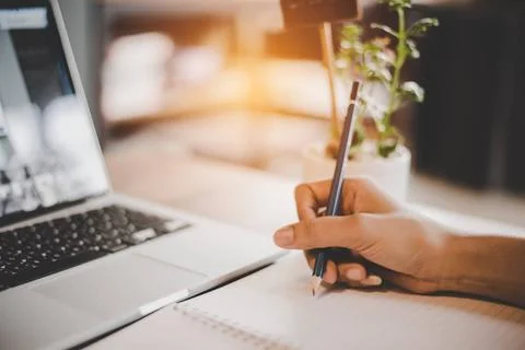 People hand using pencil to draw and noting on notepad. Laptop computer an... Stock Photos