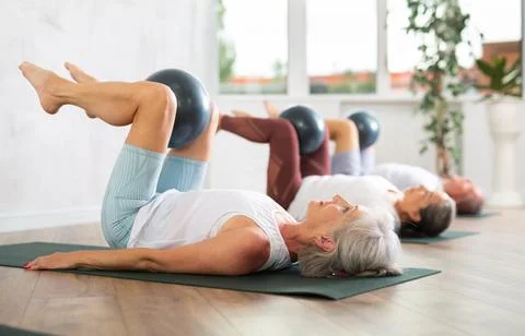 People lying on karemat, pulled bent legs to themselves and clamped soft-ball in Stock Photos