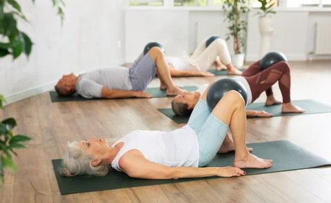 People lying on karemat, pulled bent legs to themselves and clamped soft-ball in Stock Photos