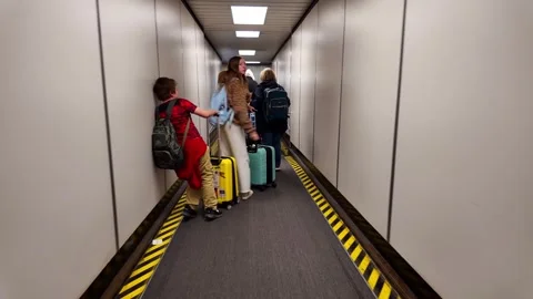People moving through a jet bridge for boarding, carrying luggage and backpacks Видео 335322212