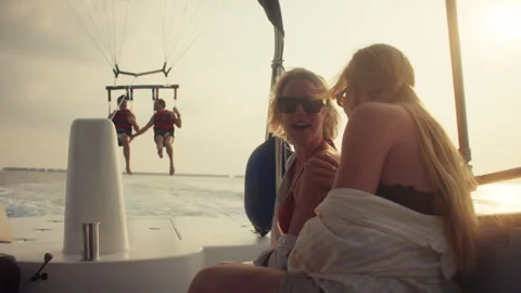 People parasailing over the ocean while friends watch from a boat during sunset Vídeos de archivo 317973985