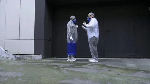 People in protective suits talking on the street in front of a huge gate Stock Footage 124955394