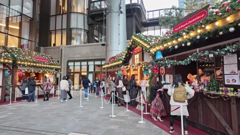 People queue at Christmas market stalls in a modern plaza. 库存影片 346011969
