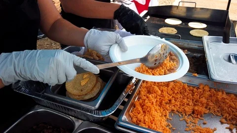 People in a queue, lifting beans and rice, on a plate, at a outdoor taco Stock Footage 116755123