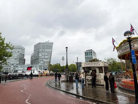 People queuing at a carousel ticket booth on a rainy day along the modern w.. Stock Photos