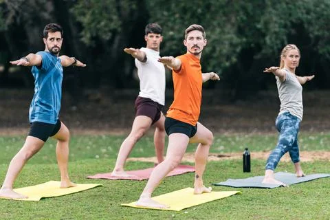 People raising arms while doing a yoga pose in a public park Stock Photos