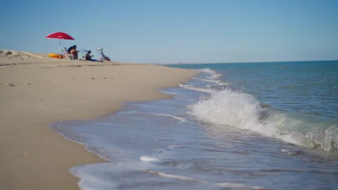 People relax on the beach while a wave crashes in slow-motion Stock Footage 164783110