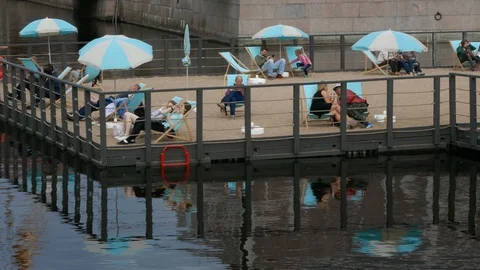 People relaxing on an artificial sandy beach made over a river inside city Video stock 103288092