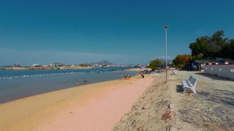 People Relaxing on Sandy Beach with White Benches by Calm Coastal Bay Stock Footage 337028184