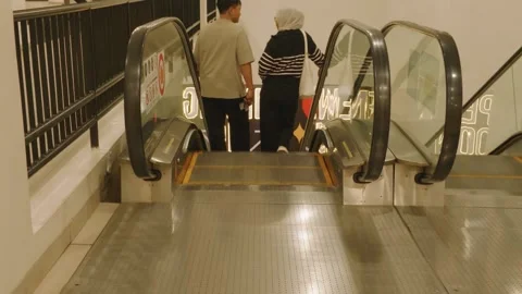 People riding down the escalator inside a modern building with glass panels. Vídeos de archivo 343418513