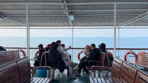 People riding ferry, inside view. Blue water outside shimmers sunlight. Stock Footage 307488378