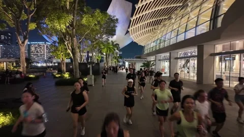 People run at the open space outside Marina Bay Sands, with city lights glowing. Видео 318099434