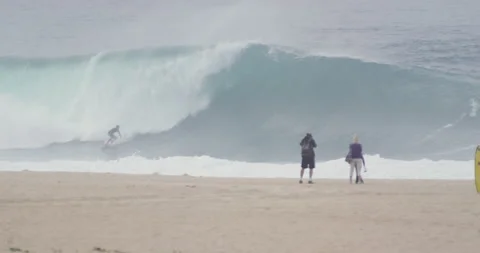 People on sandy beach looking at pro surfers riding big waves in slow motion Stock Footage 155606869