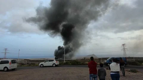 People seeing large column of black smoke from a fire in a car depot,Tenerife 4k Stock Footage 168718605