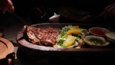 People share and cut steak at a lively dinner table with assorted dishes Stock Footage 344744555