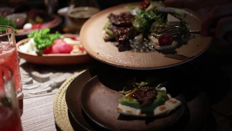 People share and cut steak at a lively dinner table with assorted dishes Stock Footage 344744803